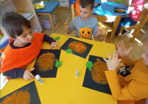 dzieci wykonują pracę plastyczną przy stolikach - stemplowane dynie
