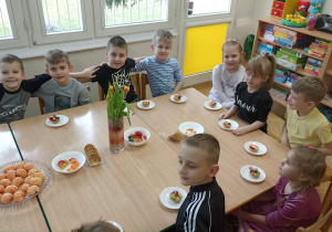 Zadowolone dzieci siedzą przed słodko zastawionym stołem.