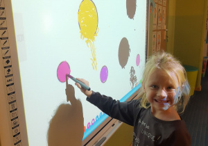 Dziewcznka kolorująca kropkę na tablicy multimedialej.