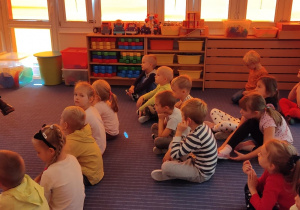 Przedszkolaki słuchające czytaniej książki.