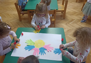 Dzieci przyklejające papierowe sylwety dłoni.