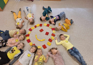 Dzieci leżące na dywanie wokół emotki uśmiechu.