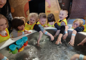 Dzieci moczą rączki przy małym zbiorniku z wodą.