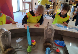 Dzieci eksperymentują przy małym zbiorniku wodnym.