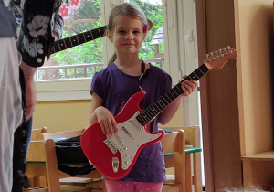 Dziewczynka próbuje grać na małej gitarze.