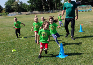 Biegające dzieci między pachołkami sportowymi.
